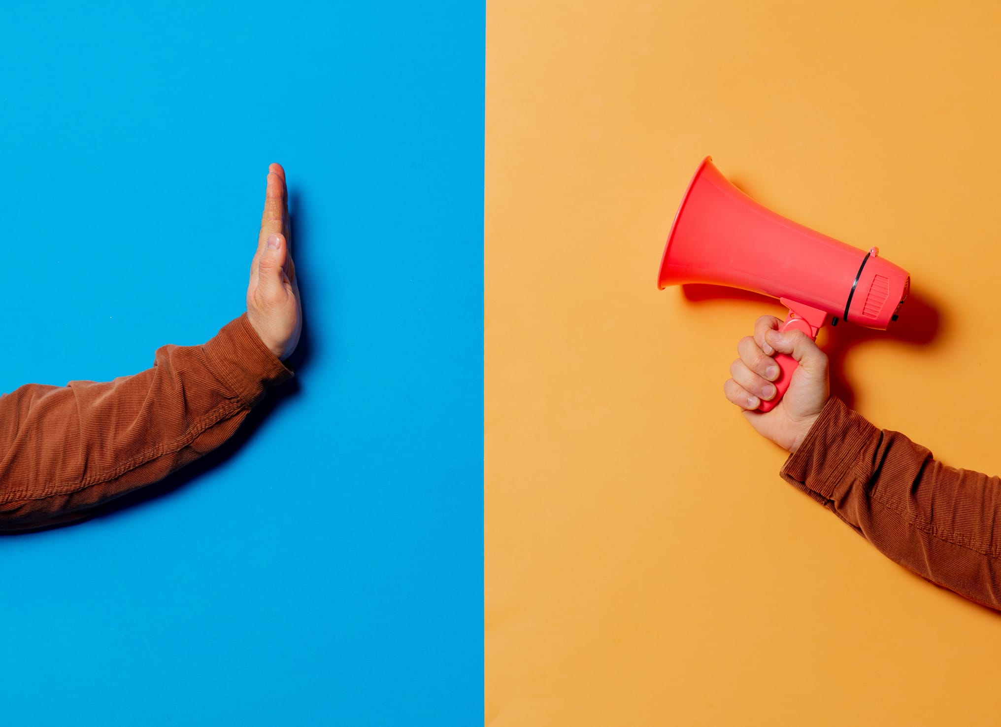 Two hands, one with megaphone and other show up stop symbol on blue and yellow backgrounds