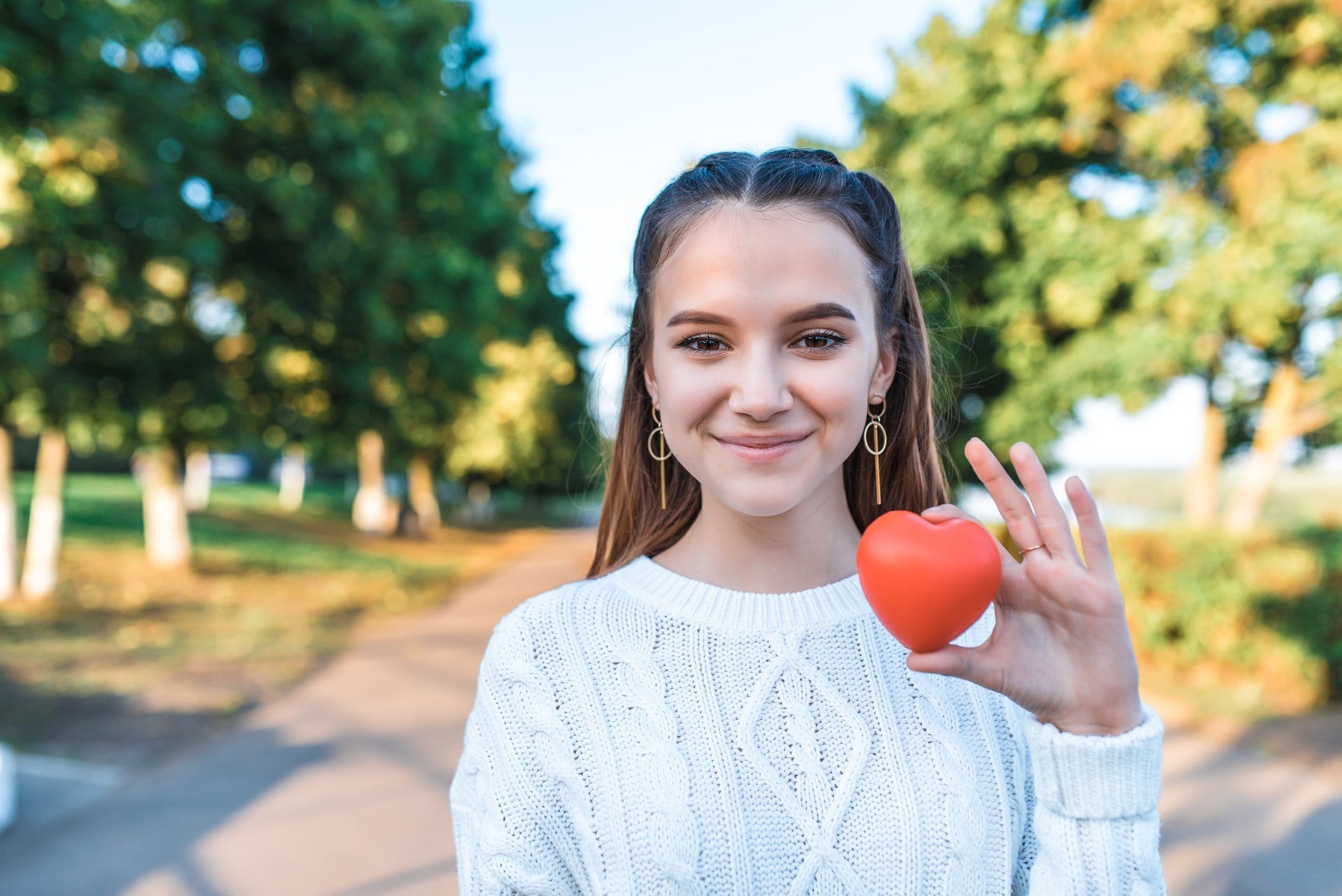 Happy cheerful teenage girl 13-15 years old, summer autumn spring in park, red heart in her hand. Free space text. Concept give love, donation wish of love, help children, save life, positive joy.