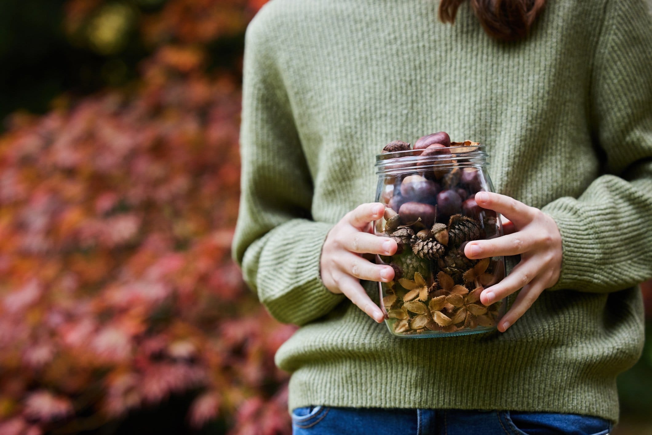 Close Up Of Girl Outdoors Holding Jar Of Autumn Pine Cones With Conkers Acorns And Beech Nut Cases