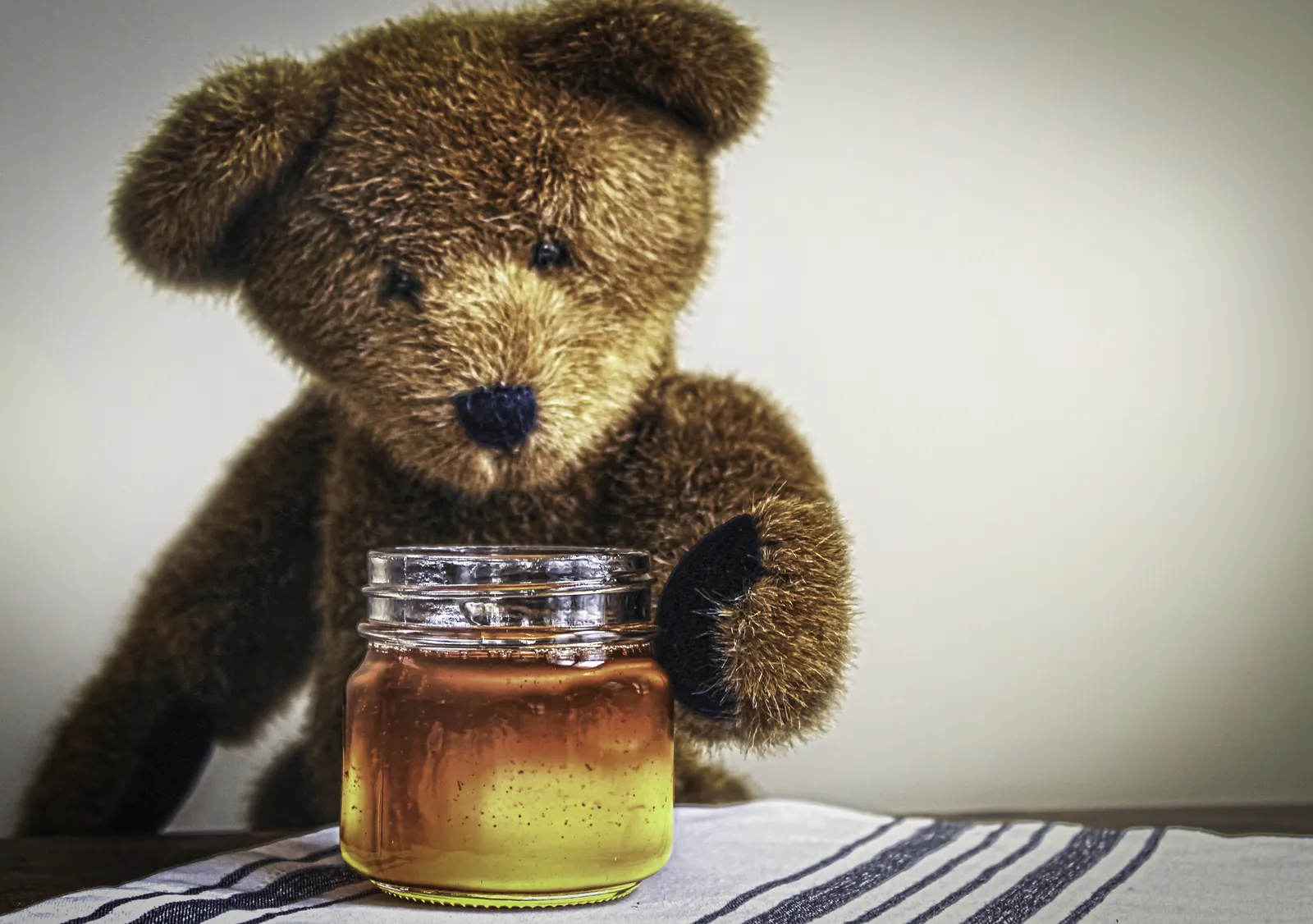 Teddy bear reaching into a jar of honey